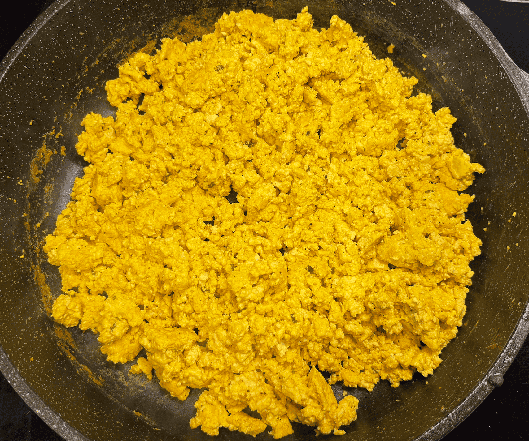 Golden vegan tofu scramble cooked in a skillet, seasoned with turmeric, garlic, and herbs, creating a fluffy, high-protein egg-free breakfast with scrambled egg texture.