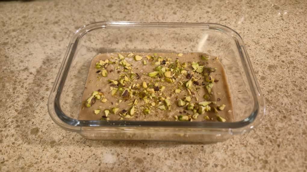 Nutty vegan pistachio halva in a glass container with crushed pistachio garnish.